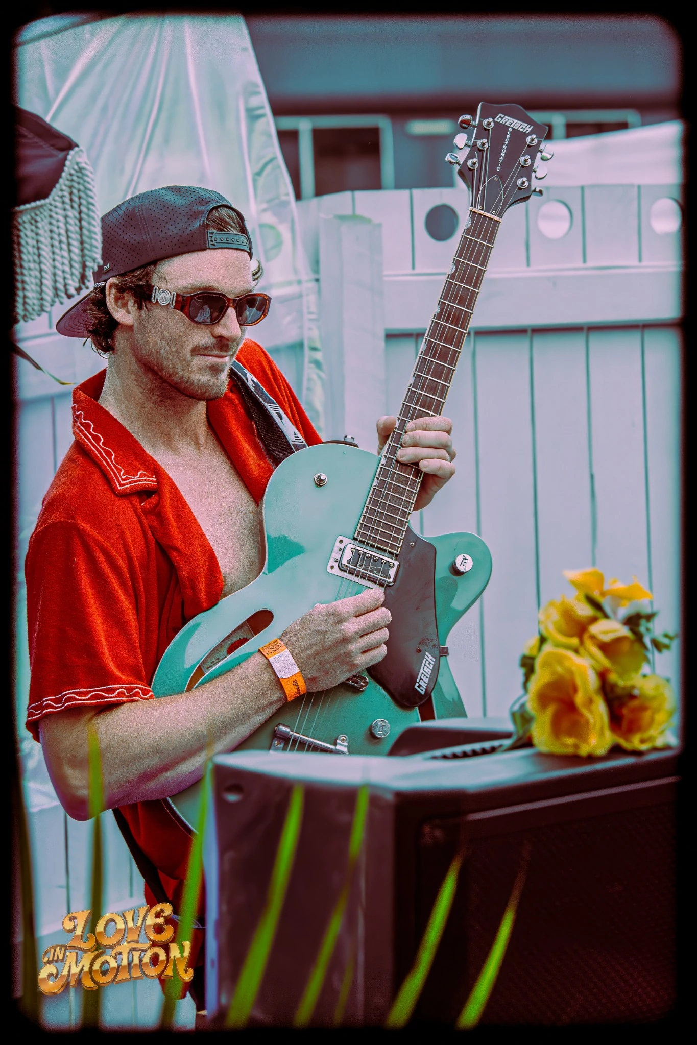 A musician in a red shirt holding his guitar at Love in Motion